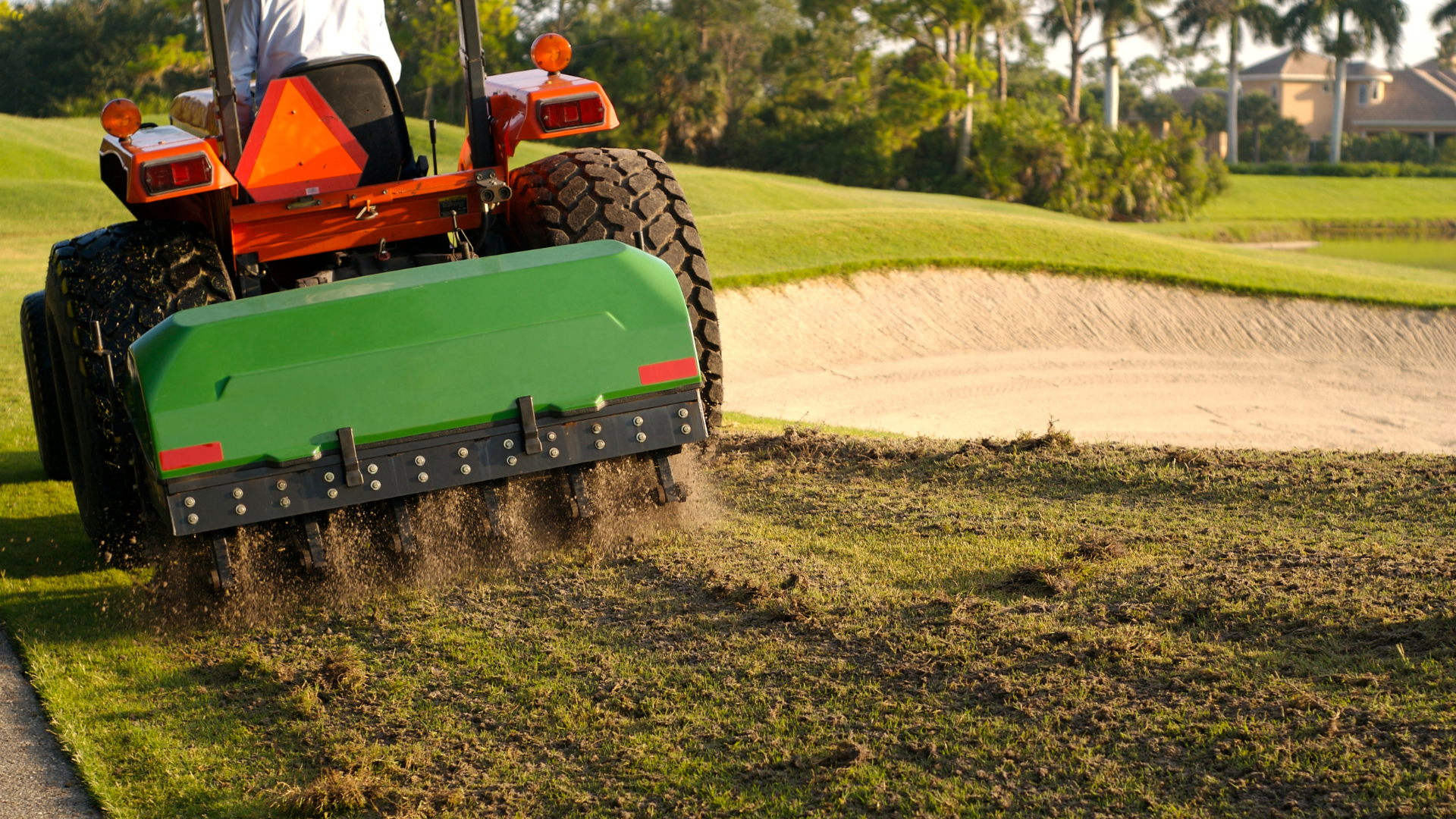 A man is driving a tractor on a golf course.