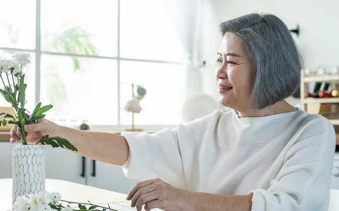 Woman holding a measuring tape and a blender filled with greens, smiling. Kitchen setting.