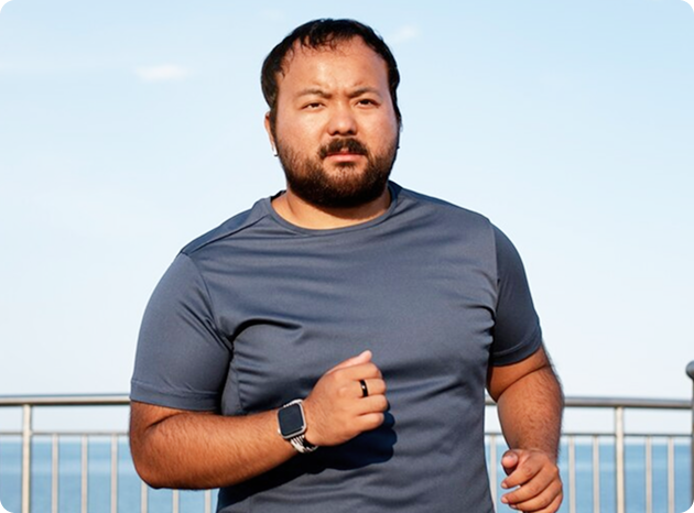 Woman holding a measuring tape and a blender filled with greens, smiling. Kitchen setting.