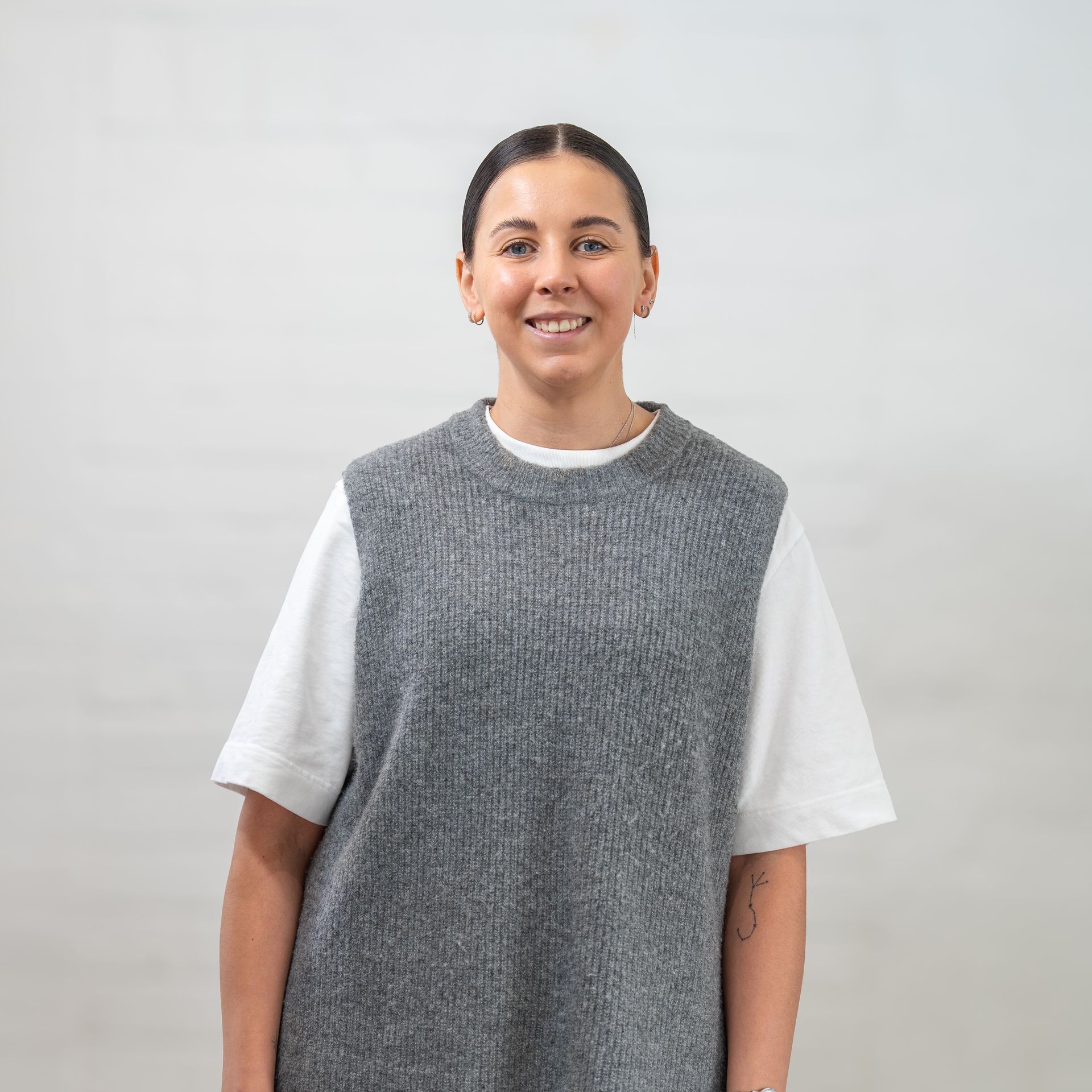 A woman wearing a grey vest and a white t-shirt is smiling.