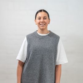A woman wearing a grey vest and a white t-shirt is smiling.