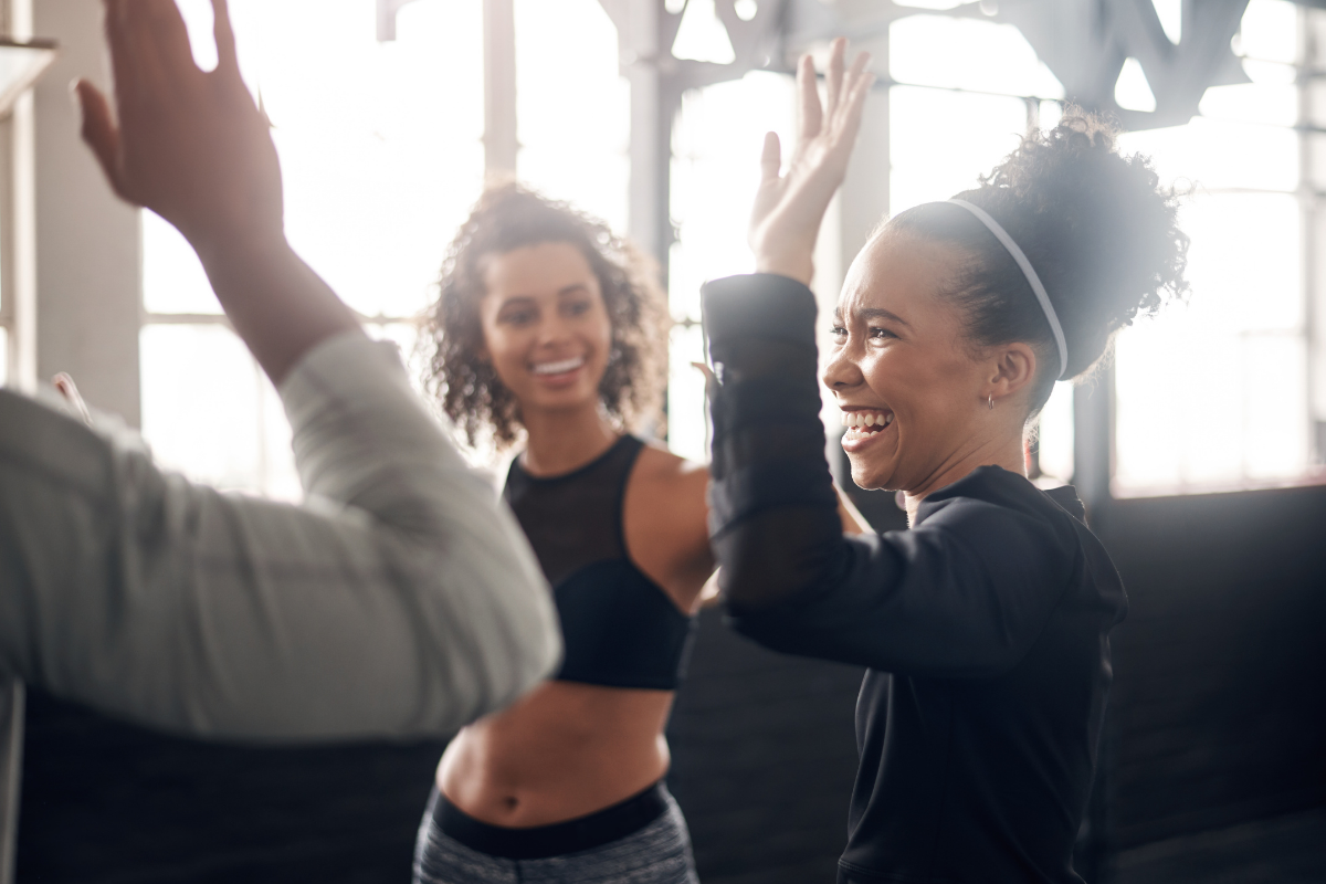 Three people in a gym smiling while giving each other high-fives.
