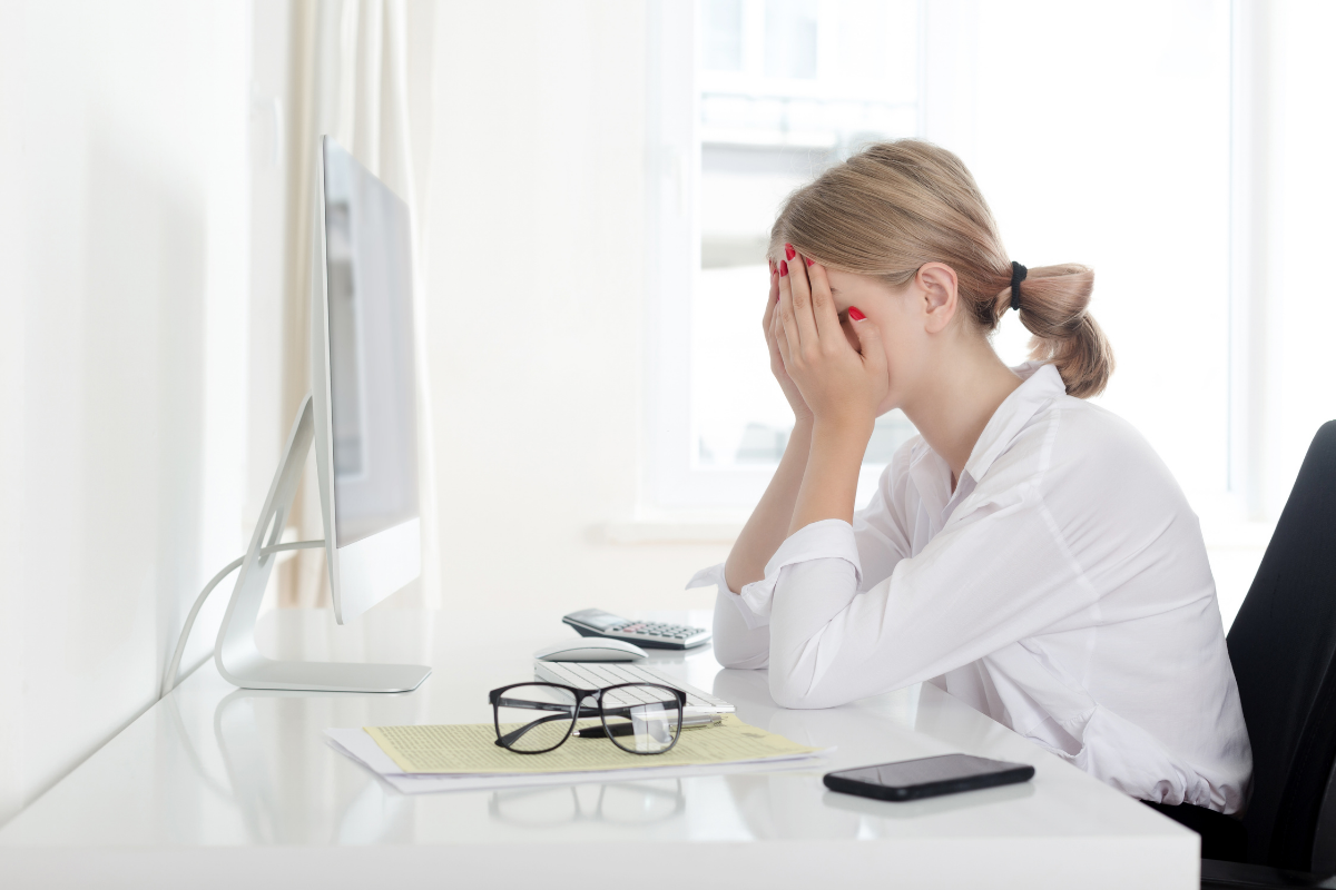 A person sitting at a desk with their head in their hands in front of a computer screen, indicating stress or frustration.
