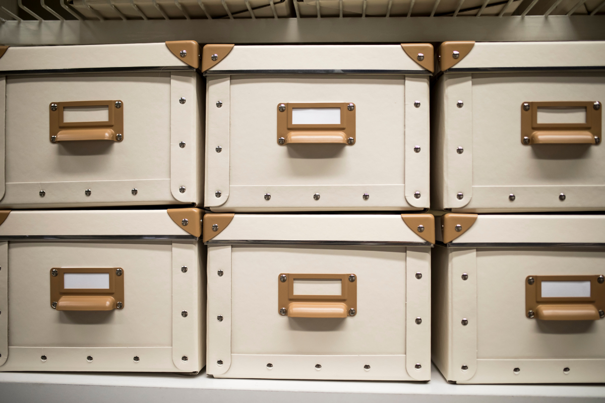 Six light-colored storage boxes with brown metal handles and corner accents, arranged in two rows of three on a shelf.