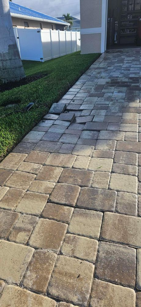 A brick walkway leading to a house with a white fence in the background.
