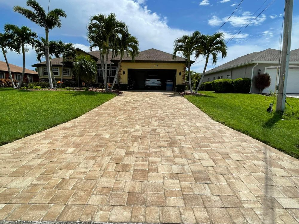 A brick driveway leading to a house with a car parked in the garage.