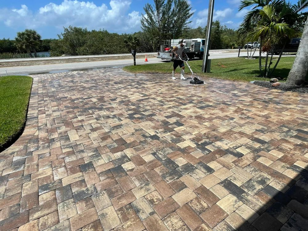 A man is cleaning a brick driveway with a broom.