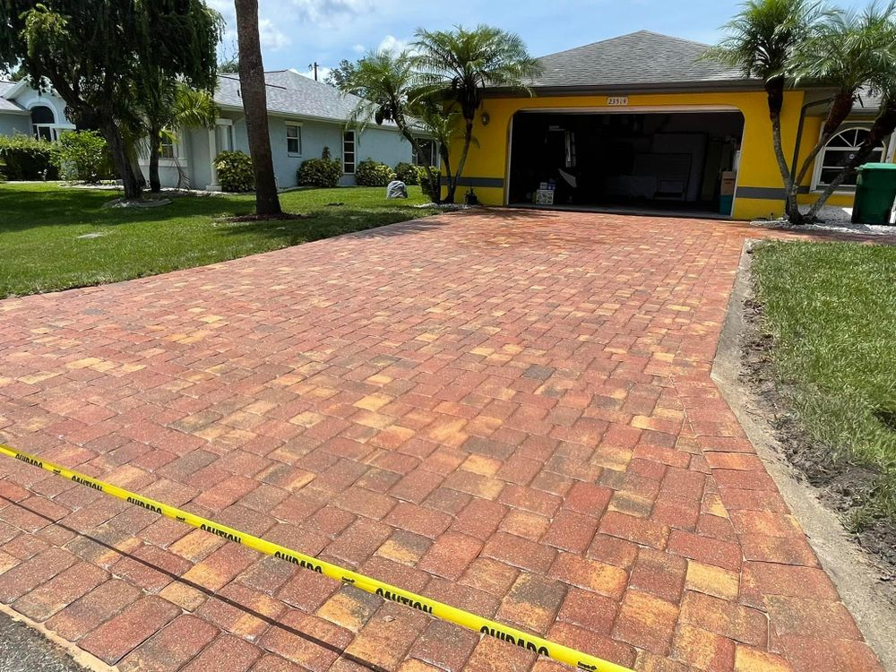 A brick driveway in front of a yellow house.