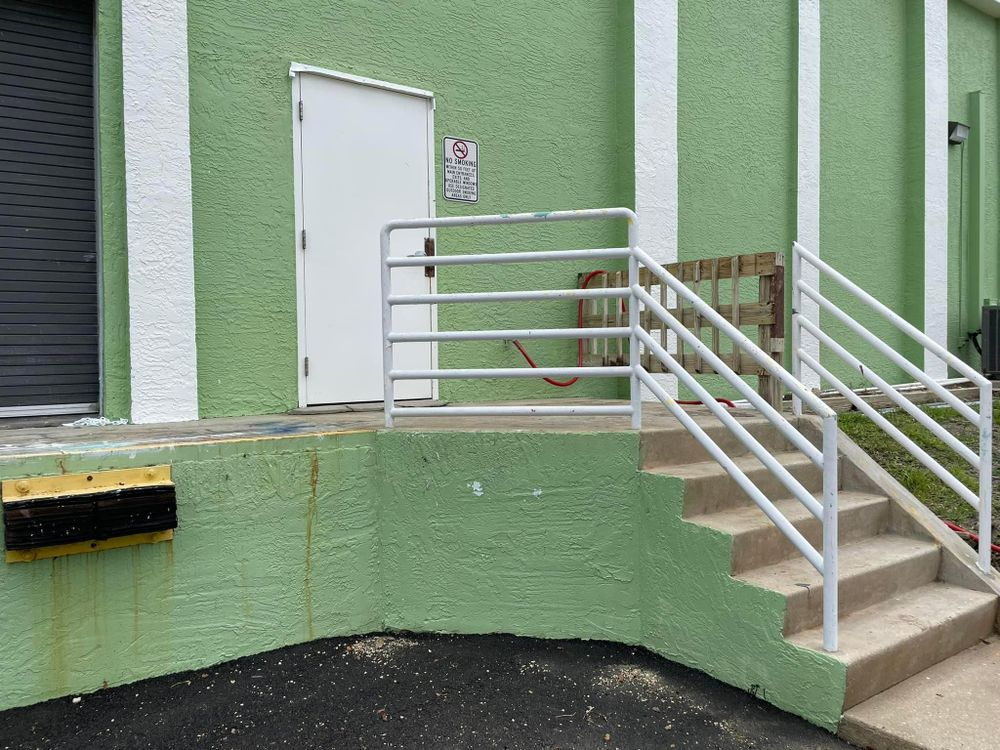 A green building with stairs leading up to it and a white railing.