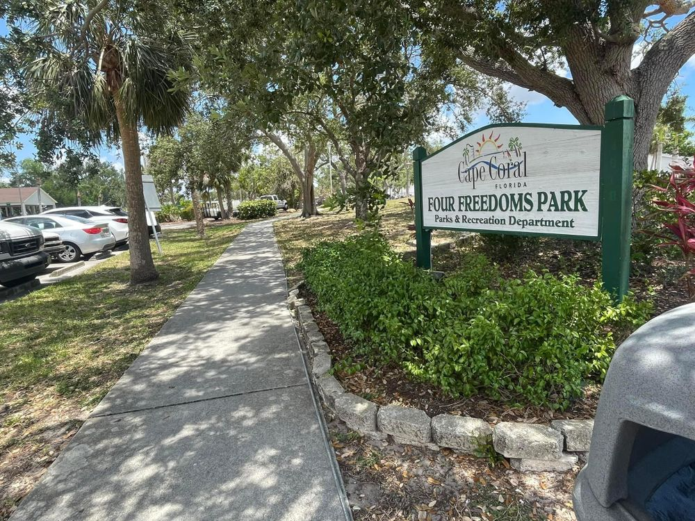 A sign for four freedoms park is sitting on the side of a sidewalk.