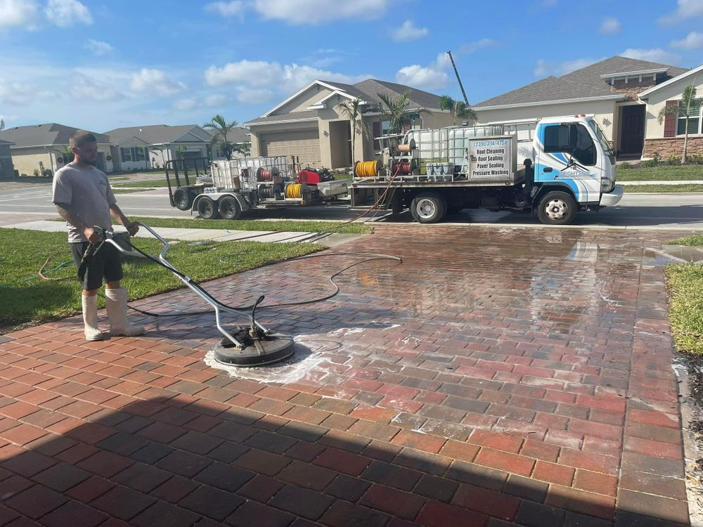 A man is cleaning a driveway with a machine in front of a truck.