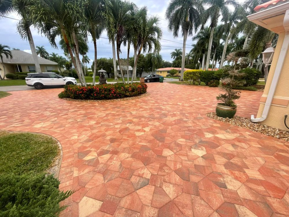 A brick driveway leading to a house with palm trees in the background.