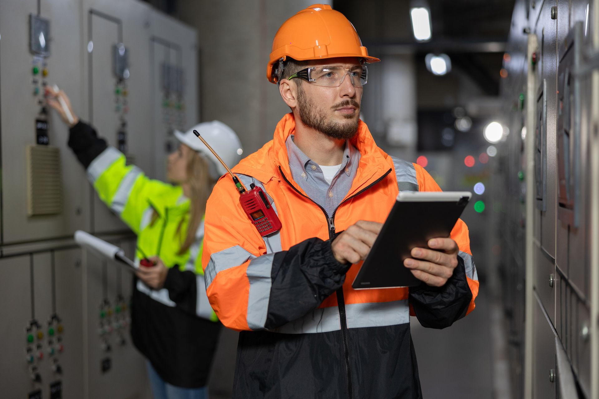 Two Caucasian electricians working with a computer and a tablet in a main electric control room. 