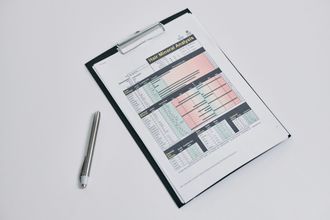 A clipboard with a spreadsheet on it next to a pen.