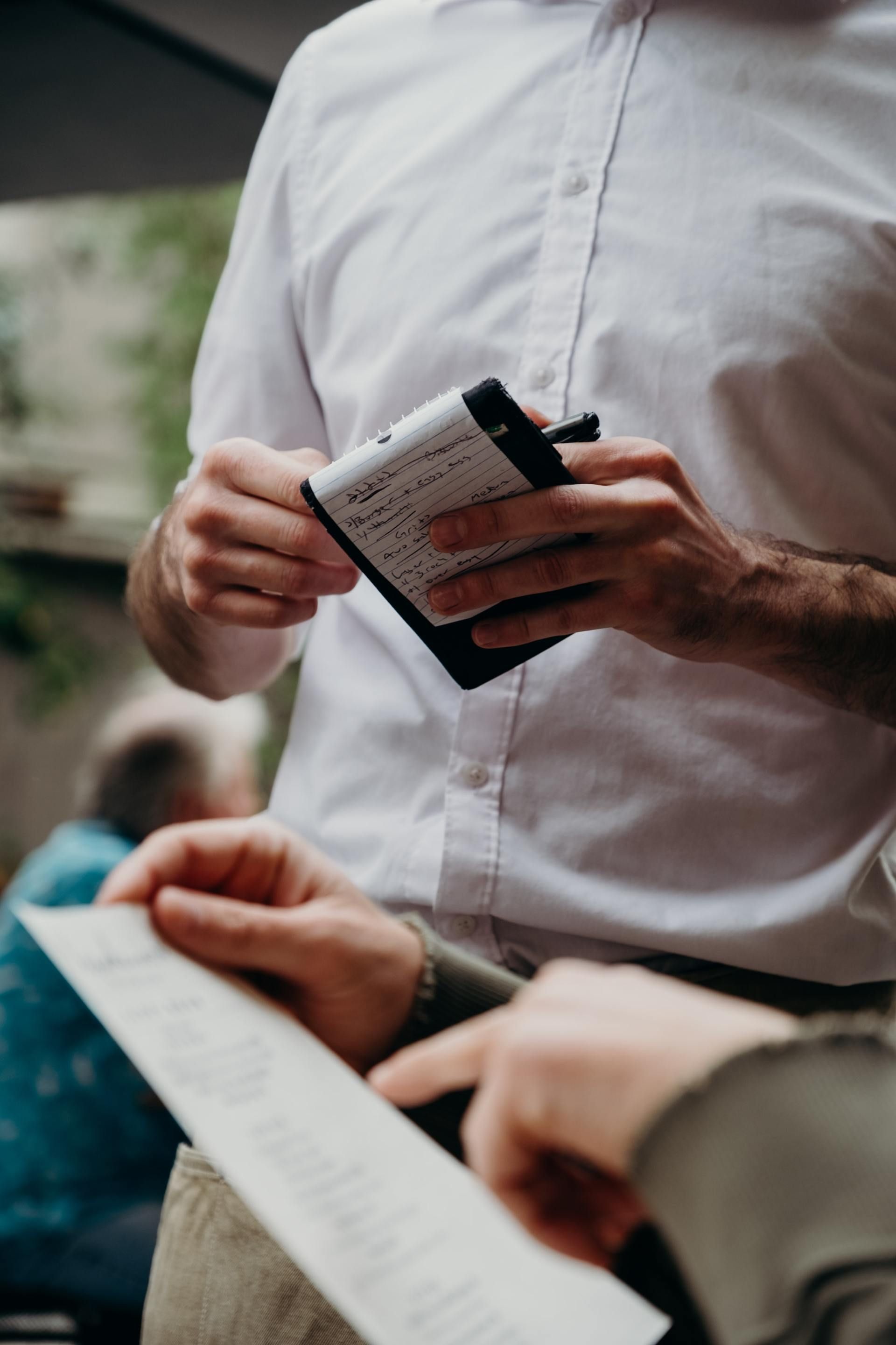 A man in a white shirt is holding a notepad and a pen.