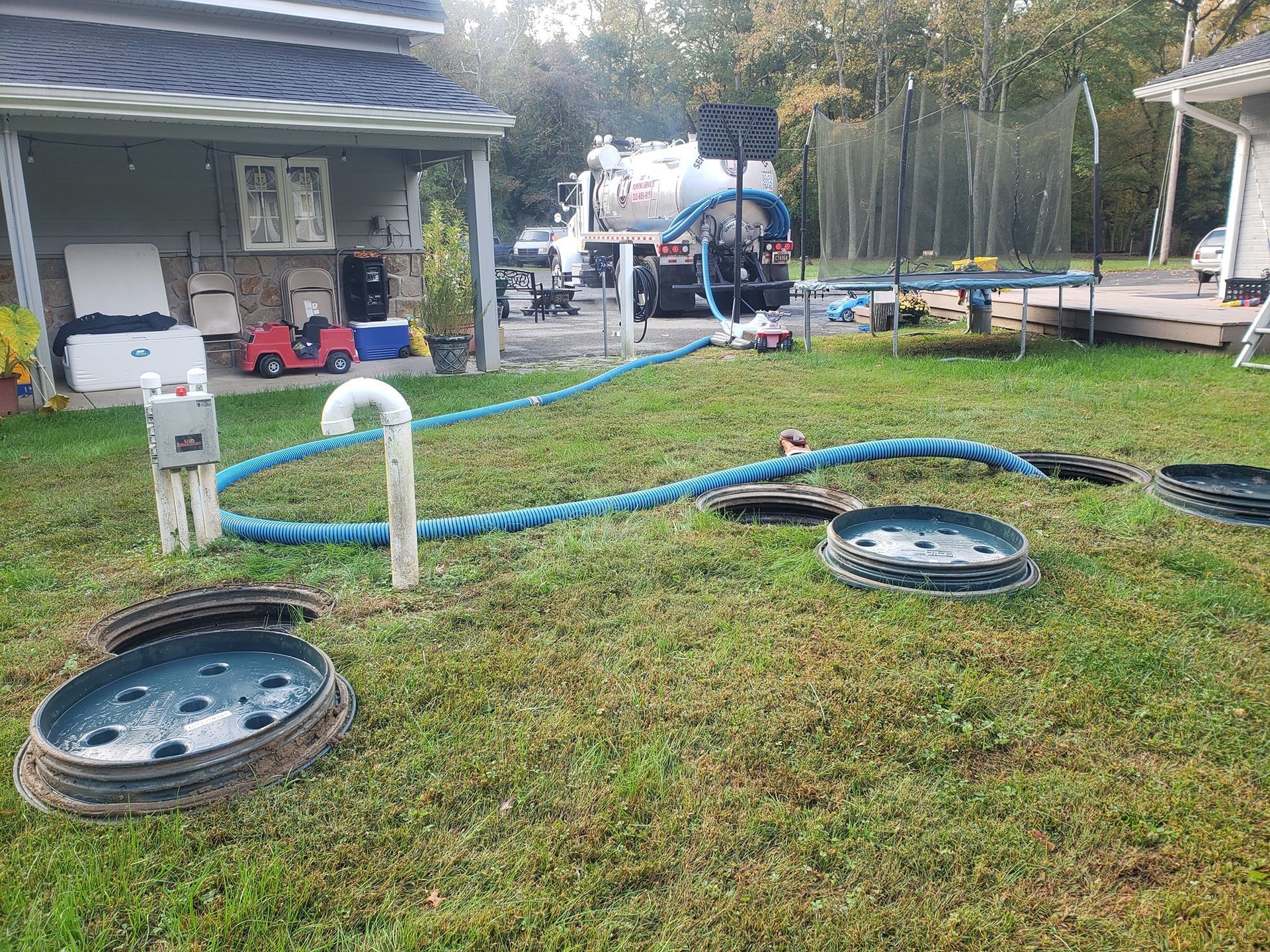 Septic tank service in a yard; hose connected to pump truck, open tank lids, and equipment.