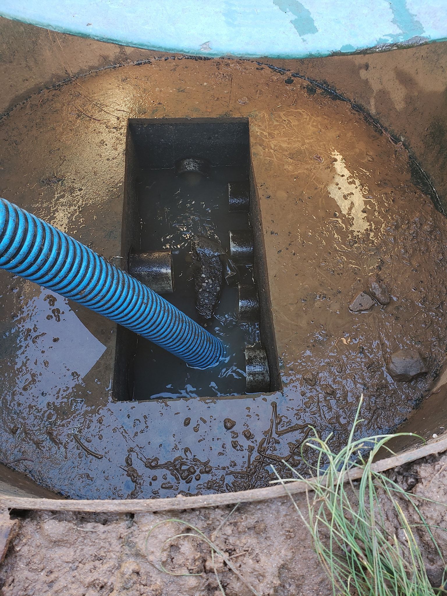 Blue hose pumping liquid waste from an open septic tank.