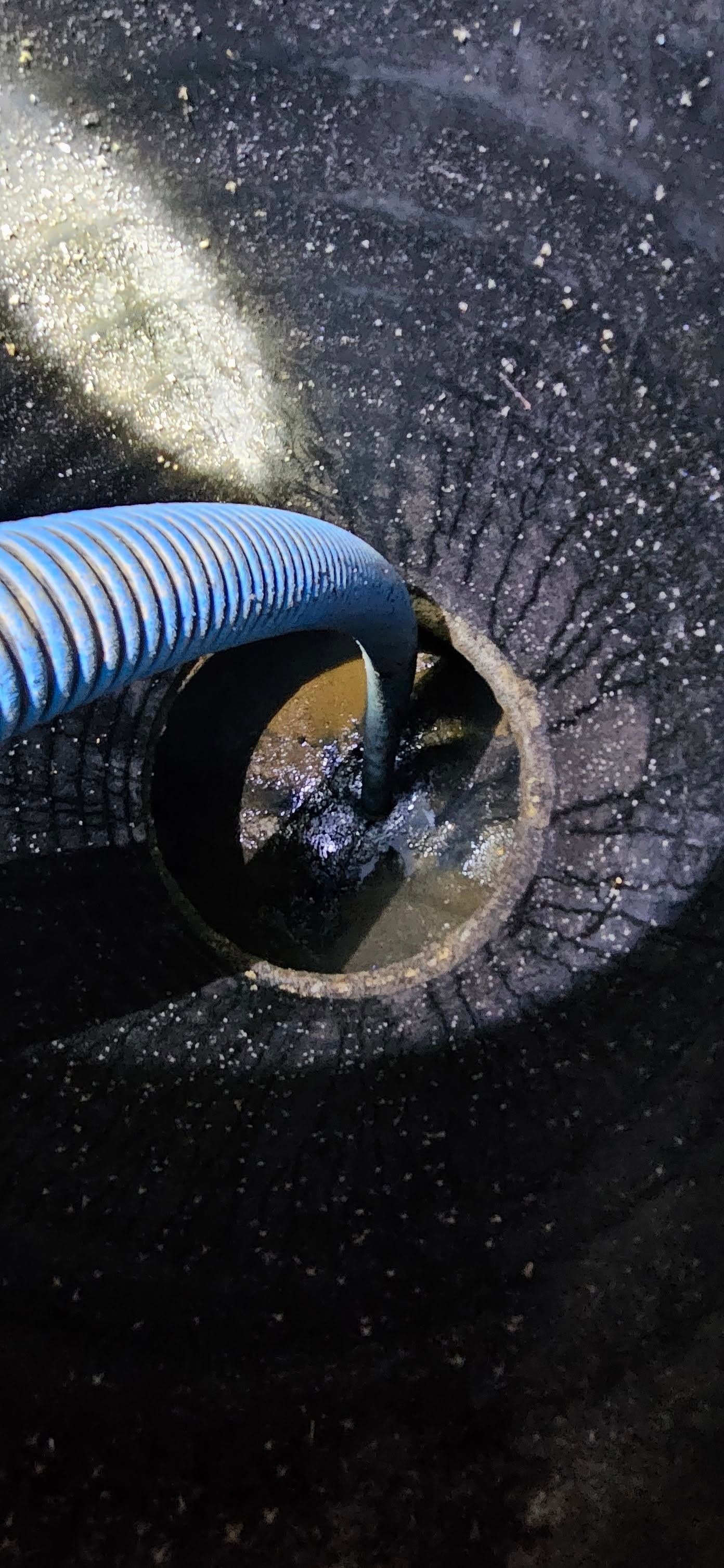 Worker with orange glove lowers pipe into an open sewer. Gray sewer grate and equipment visible. Worker with orange glove lowers pipe into an open sewer. Gray sewer grate and equipment visible.