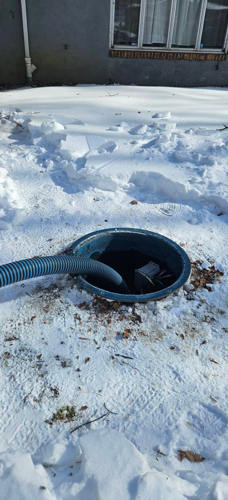 Person in boots holding a red and black water pump in muddy water, connected to a hose. Person in boots holding a red and black water pump in muddy water, connected to a hose.