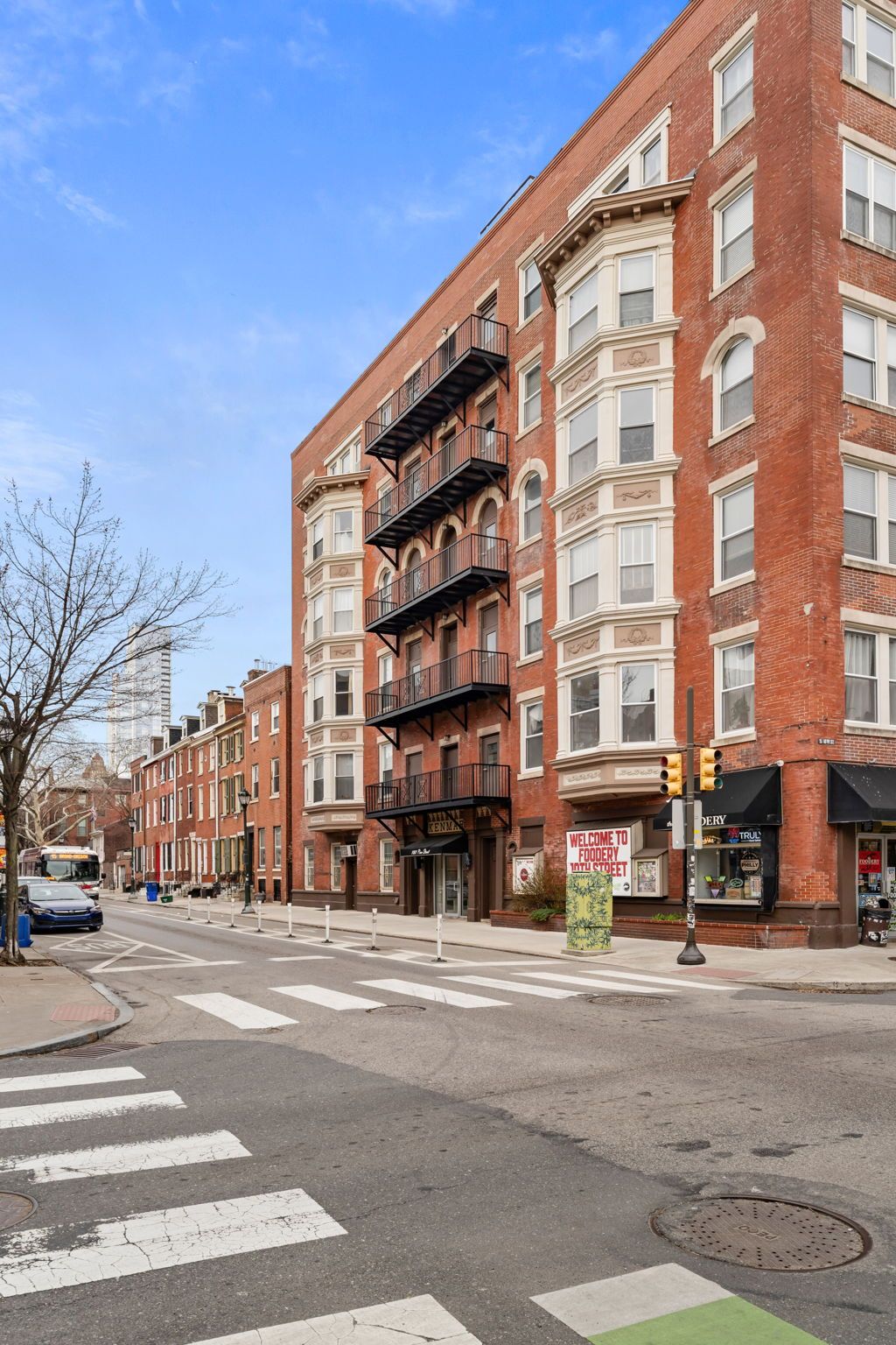 A multi-story red brick apartment building with bay windows and fire escapes on a street corner in a city.