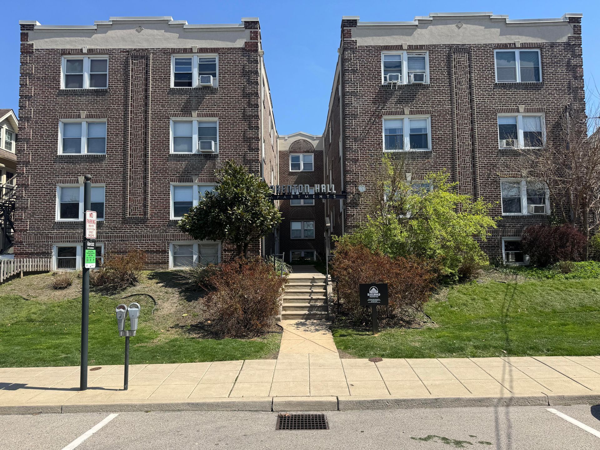Red brick apartment building with rectangular windows against a blue sky with clouds.