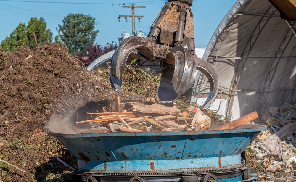 A crane is loading wood into a dumpster.
