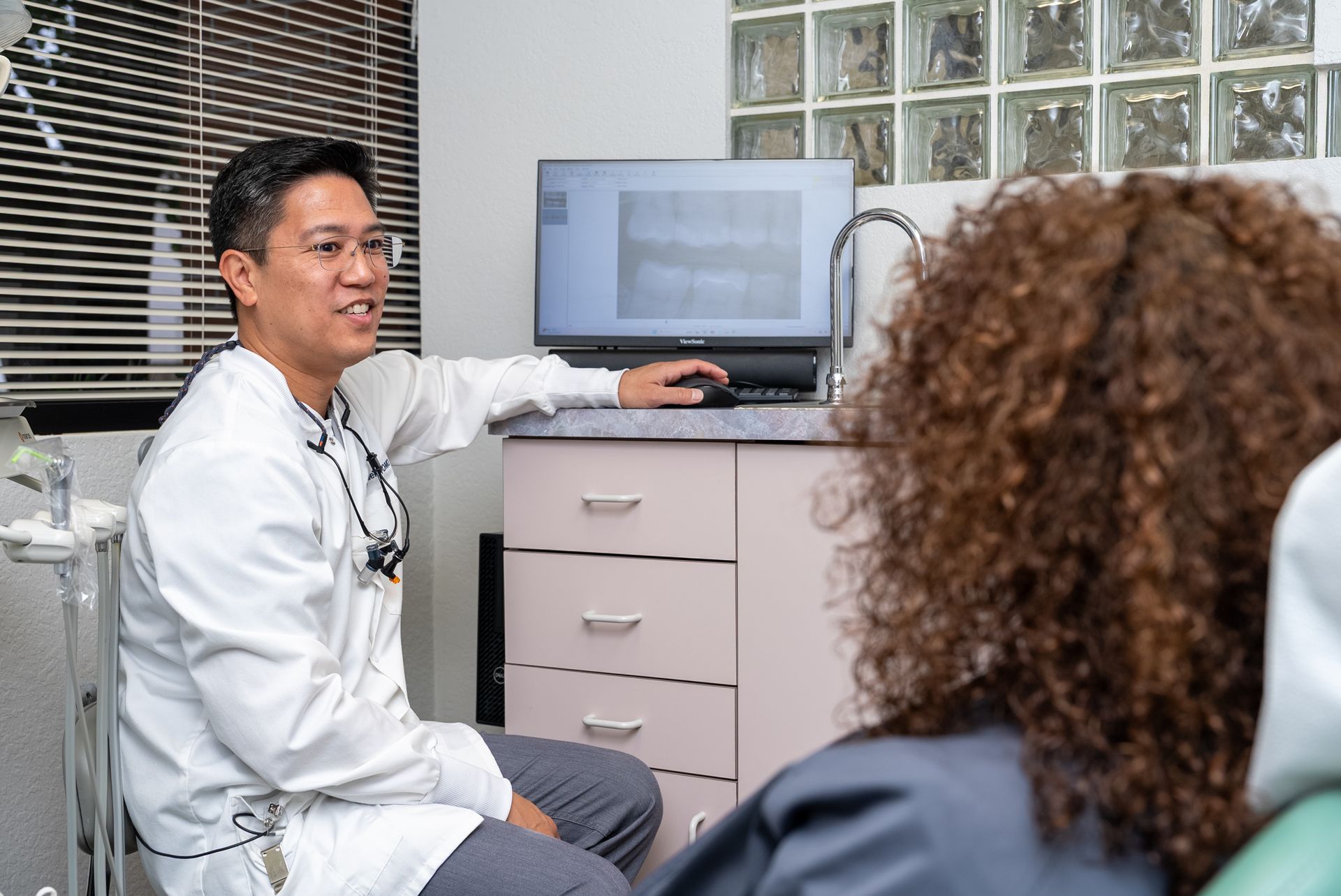 Dentist pointing at x-ray on monitor, consulting with a patient in a dental office.