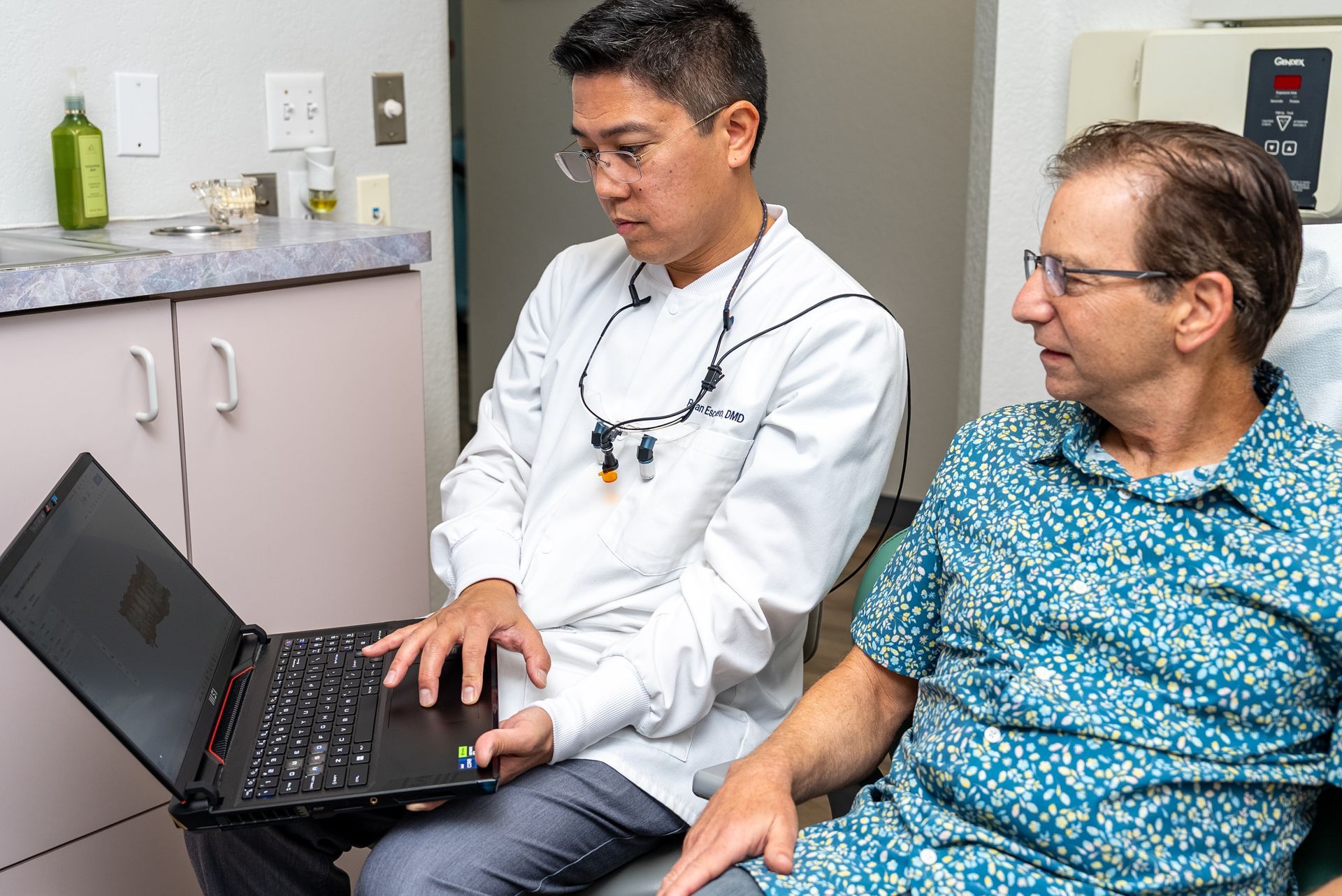 Dentist showing a patient something on a laptop. They are in an office setting.