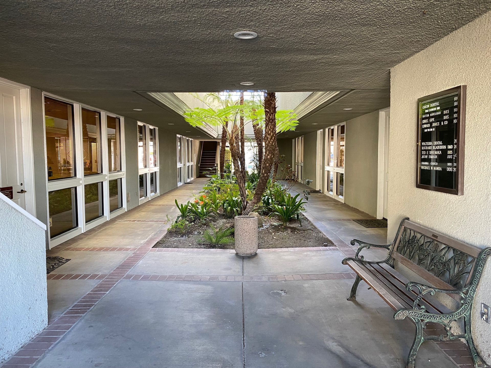 Covered walkway with windows, a bench, and a small garden with plants.