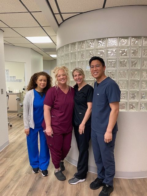 Four people in scrubs pose in a dental office hallway.