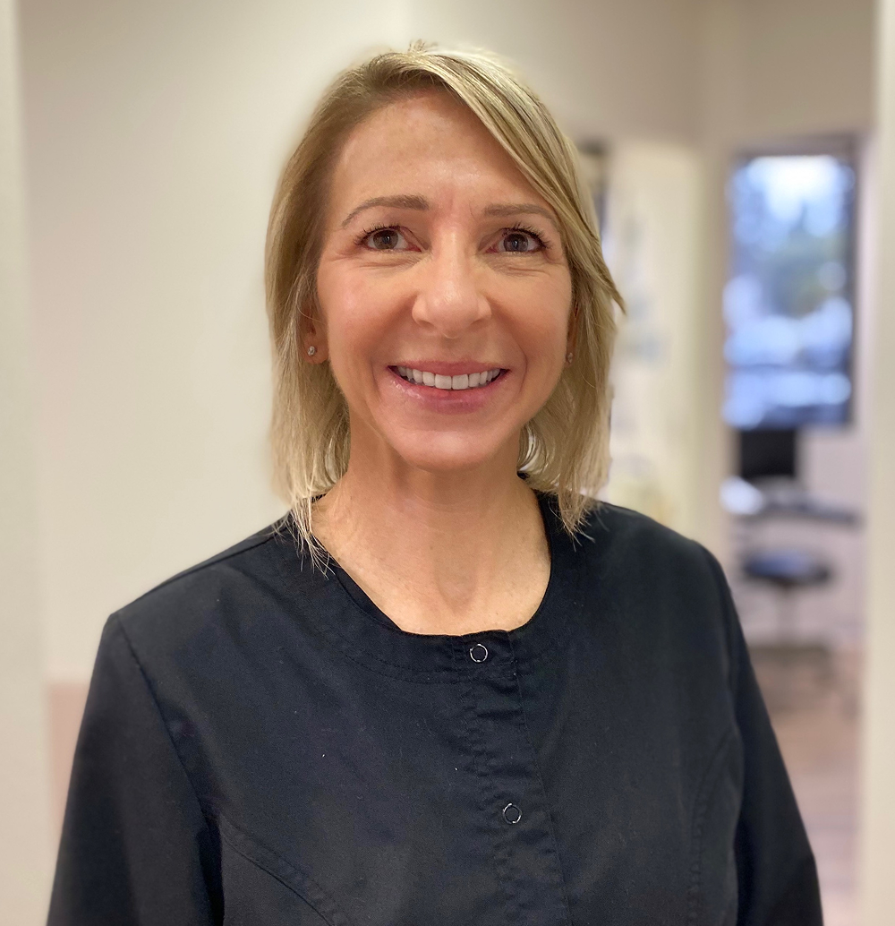 Woman with blonde hair wearing a black top smiles in a clinic setting.