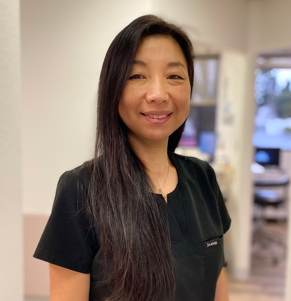 Woman with long dark hair smiles at the camera, wearing a black shirt in a well-lit interior setting.