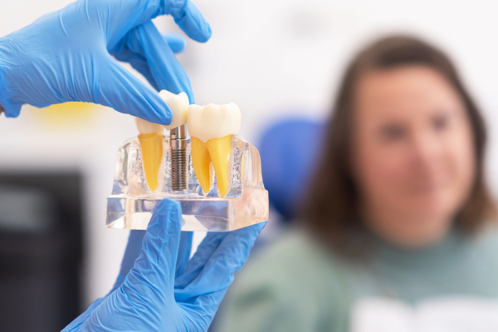 Dentist holding a model of teeth implants, explaining it to a blurred patient in a dental office.