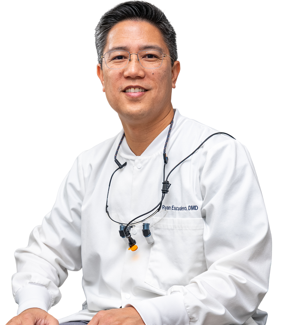 Dentist wearing loupes, smiling, in white coat.