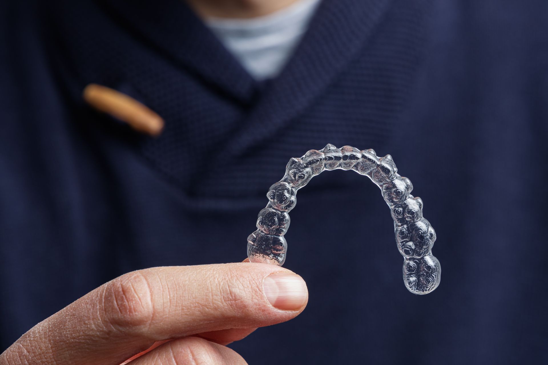 Person holding a clear aligner tray; blue sweater in background.