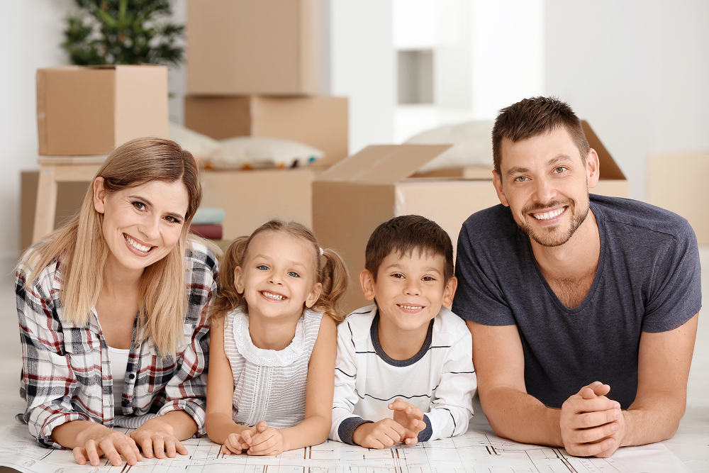 Family smiling, lying on floor in a new home with moving boxes in the background.