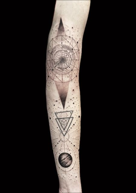 Geometric tattoo on arm: diamond, triangles, circles, and dots, black ink on skin.