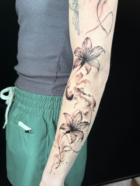 Arm with black and brown lily tattoo. The person is wearing grey tank top and green shorts.