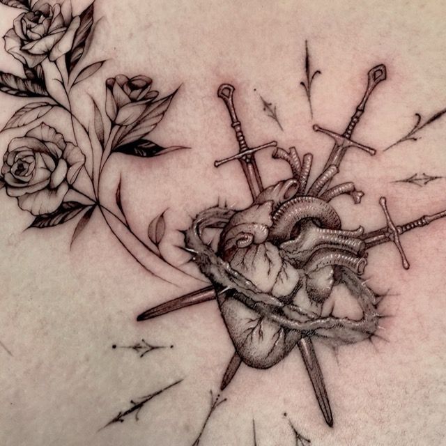 Tattoo of a heart pierced by swords, encircled by thorns, roses on the left.