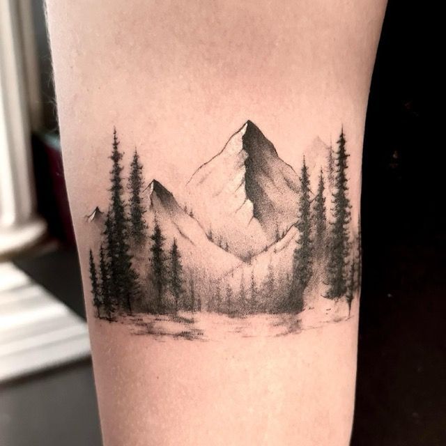 Black ink mountain and forest tattoo on skin.