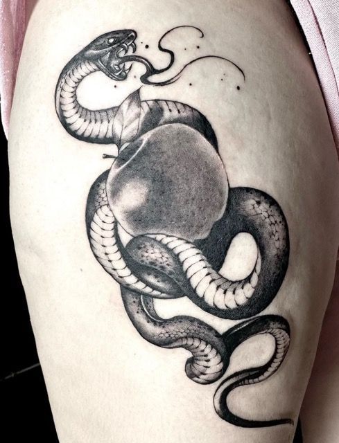 Black and white tattoo of a snake coiled around an apple; snake's tongue out, on a person's thigh.