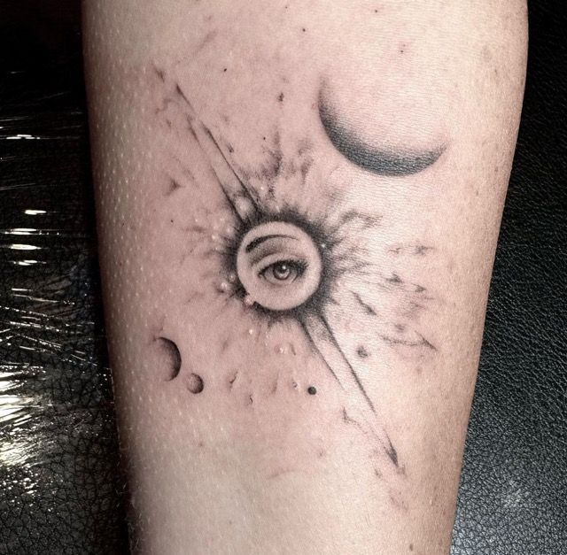 Tattoo of a sunburst with an eye, two moons, and stars.
