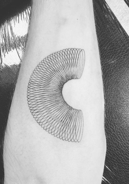 Black and white tattoo of a coiled, arc-shaped spring on a pale forearm.