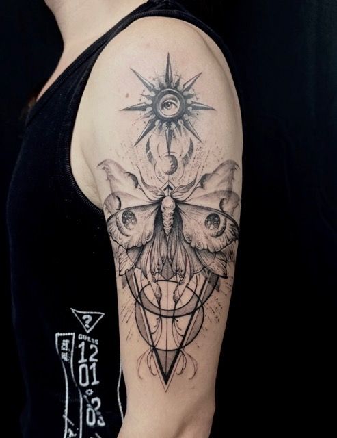 Black and white tattoo on arm, featuring a moth with sun and geometric shapes.