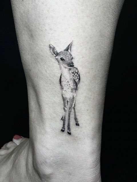 Black and white tattoo of a fawn standing on a person's ankle.