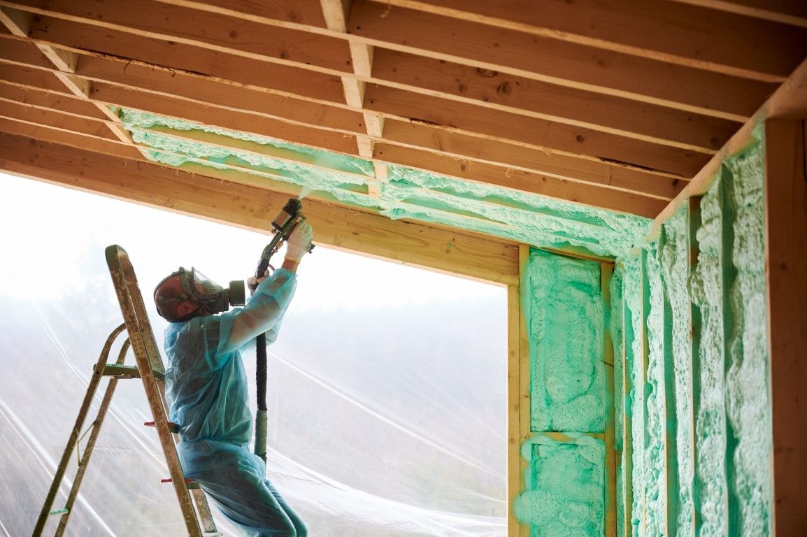 Worker spraying green insulation on attic ceiling beside a ladder
