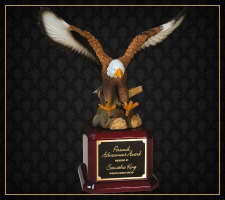 A statue of an eagle with its wings outstretched is on a plaque that says home of achievement award