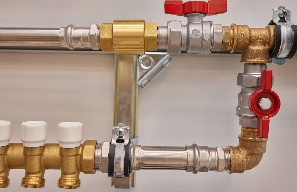 Plumbing Pipes and Valves Against a White Wall. Two Red Handled Valves Are Visible — D & E Milner Plumbing In The Palms, QLD