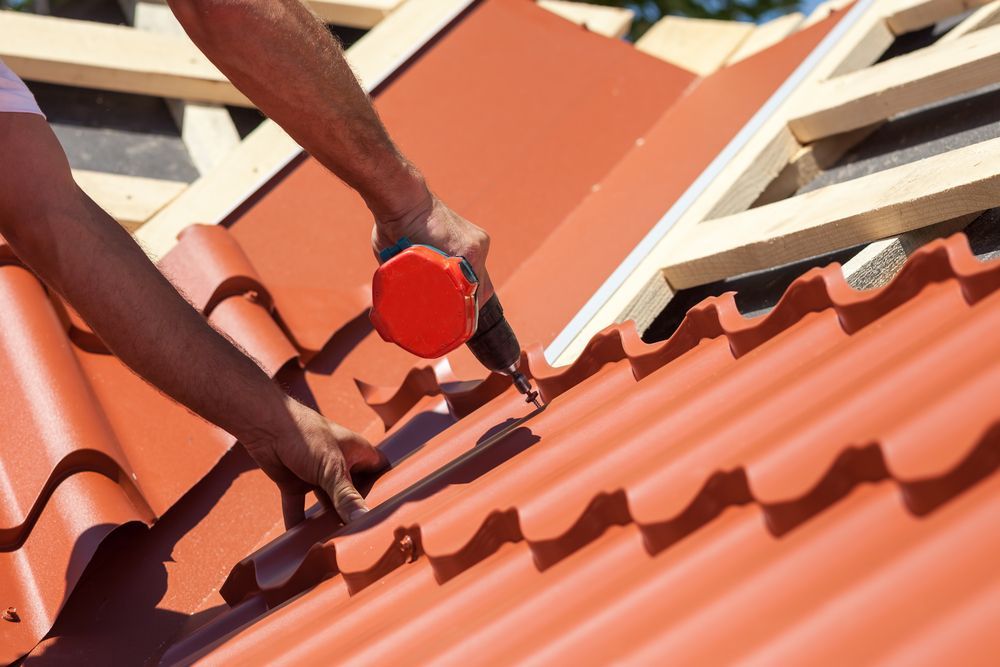 Person Using a Power Tool to Install Red Ceramic Roof Tiles on a House — D & E Milner Plumbing In The Palms, QLD