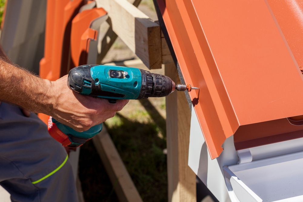 Person Using a Teal Drill to Attach Orange Roofing Material to a Structure — D & E Milner Plumbing In The Palms, QLD
